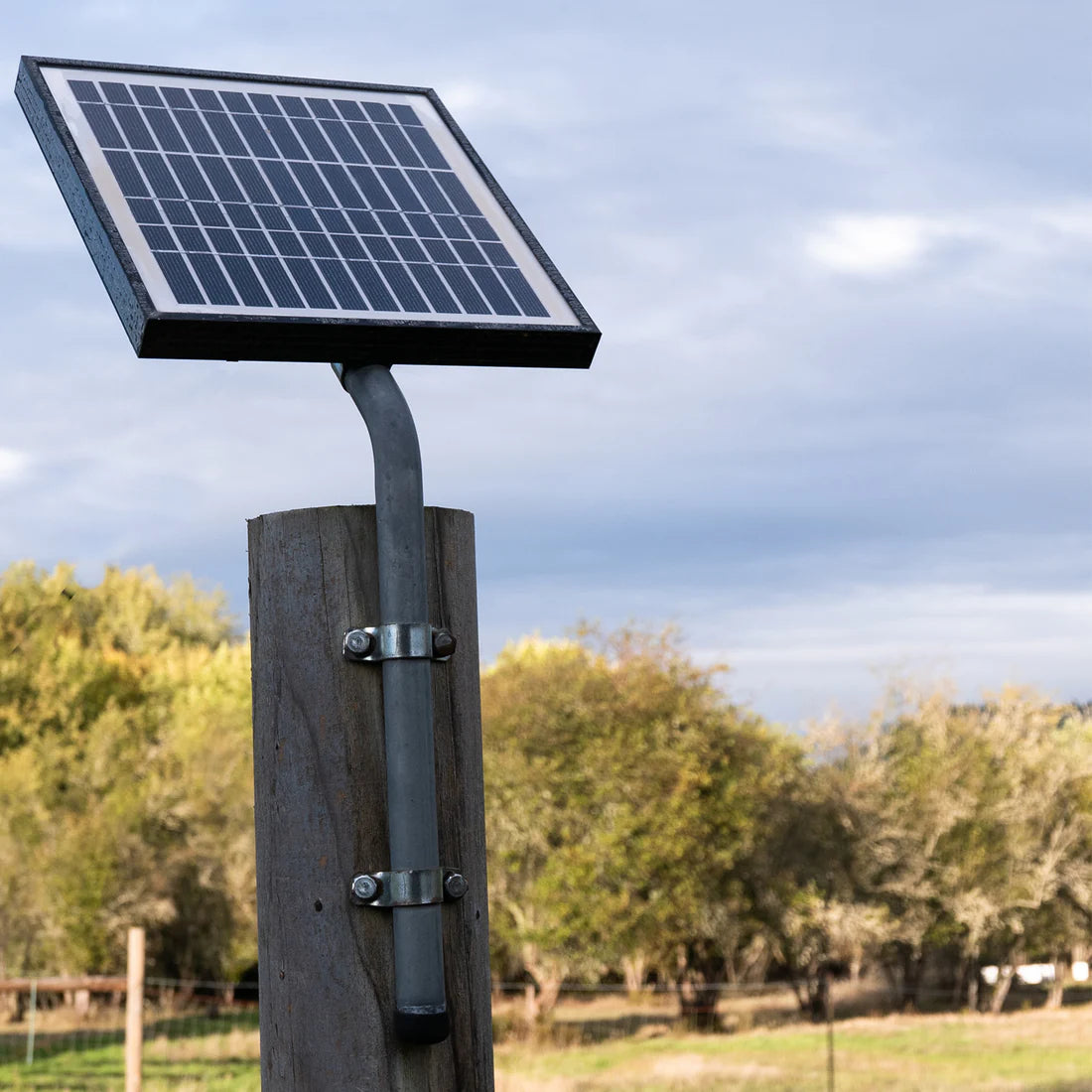 Solar panel attached to a wooden post with a scenic background of trees and sky.