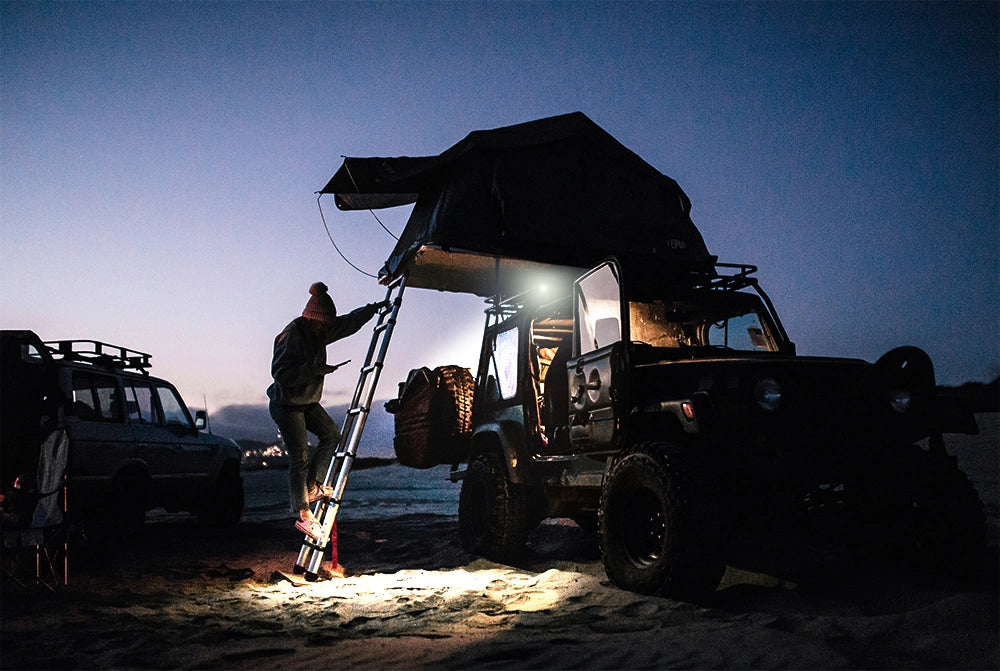 Person climbing a ladder onto a vehicle with an open roof at night lit by the Noxsolis 3" LED Slim Work Light 12-24V 24W