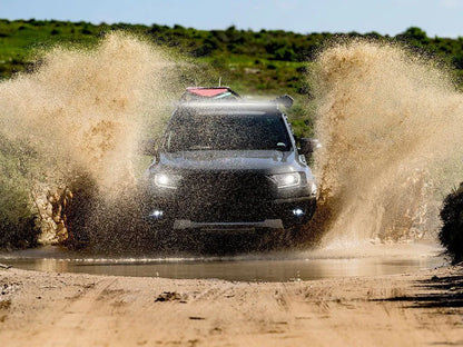 SUV driving through a muddy water puddle on a dirt road