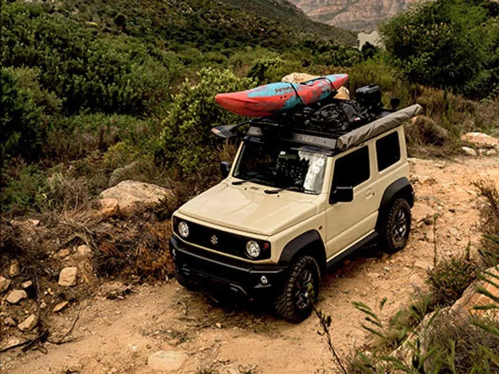Beige SUV with a kayak on top driving through a mountainous landscape