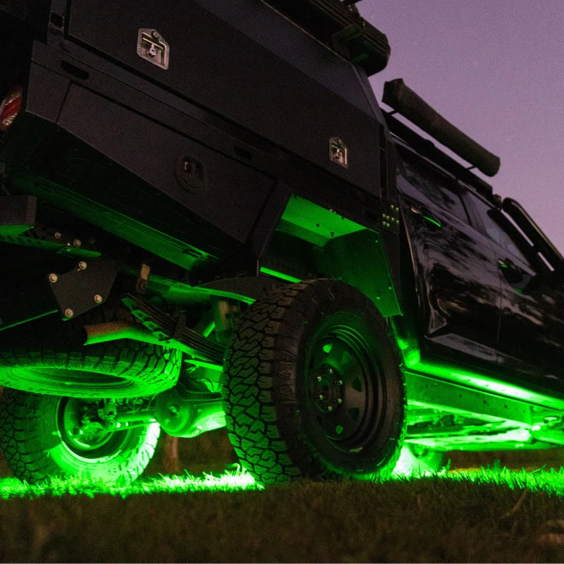 Black off-road vehicle with green underglow rock lighting on a grassy area at night.