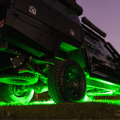 Black off-road vehicle with green underglow rock lighting on a grassy area at night.